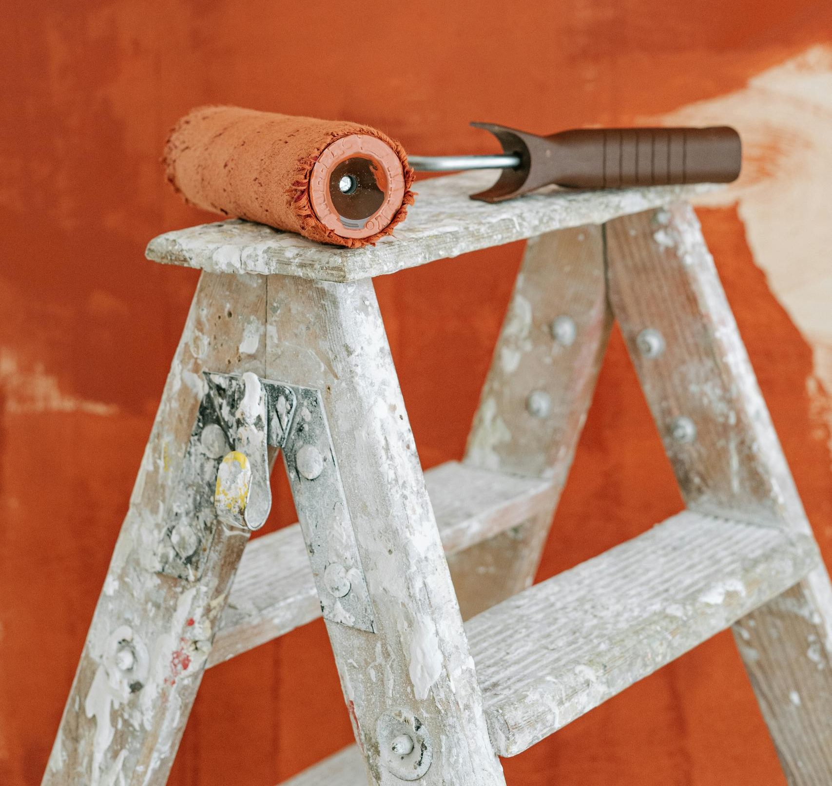 A paint roller on a stepladder against a partially painted wall, signifying home improvement.